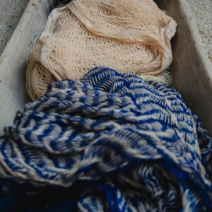 Close-up of various textured fabrics in a rustic wooden container highlighting intricate patterns.